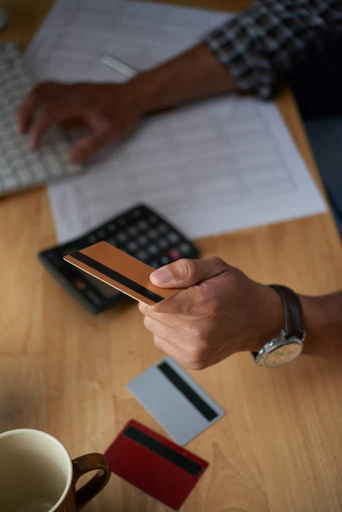 Homme en train de taper sur un clavier d'ordinateur avec une carte de crédit à la main.