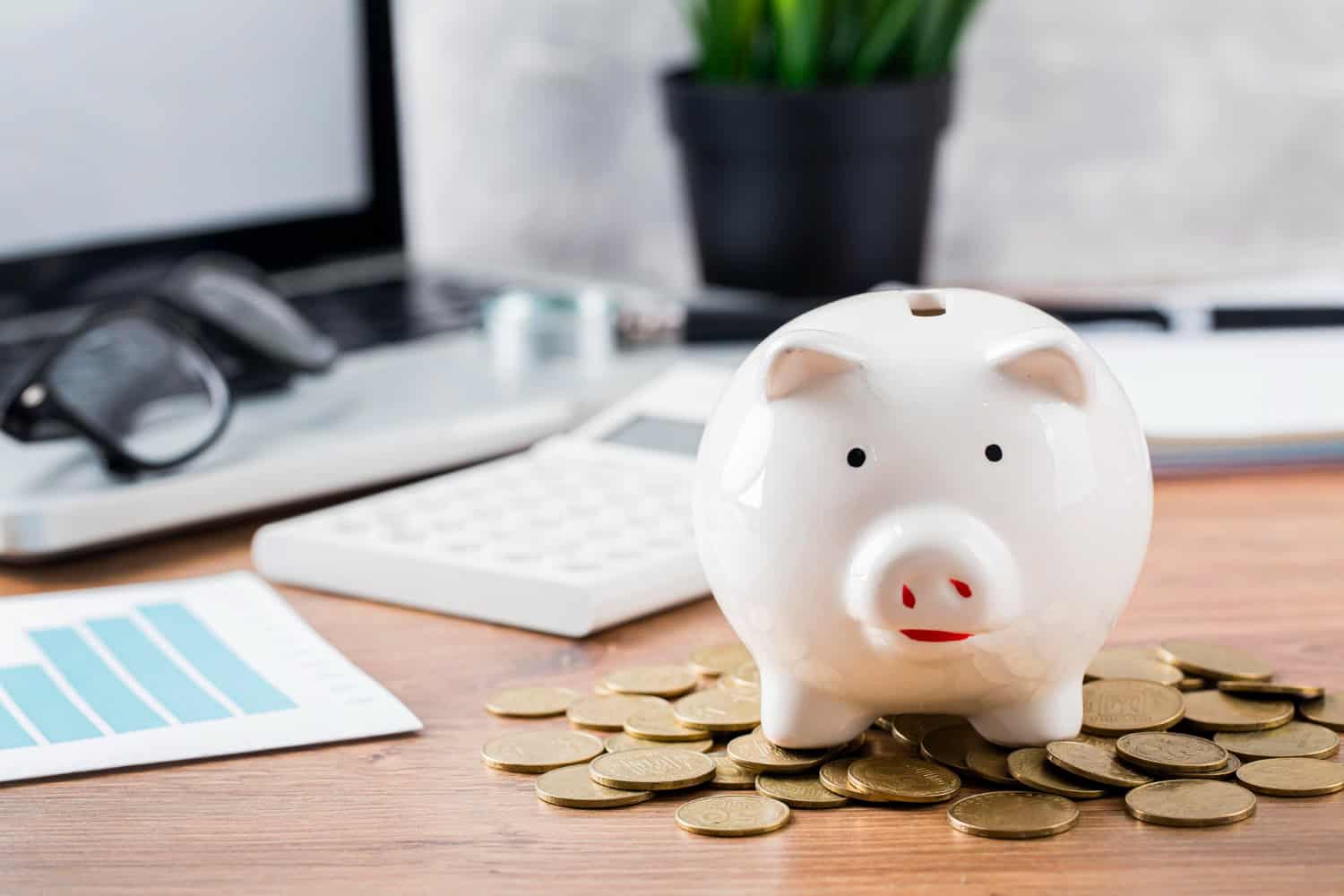 Une tirelire cochon posée sur des pièces de monnaie avec une calculatrice à côté.