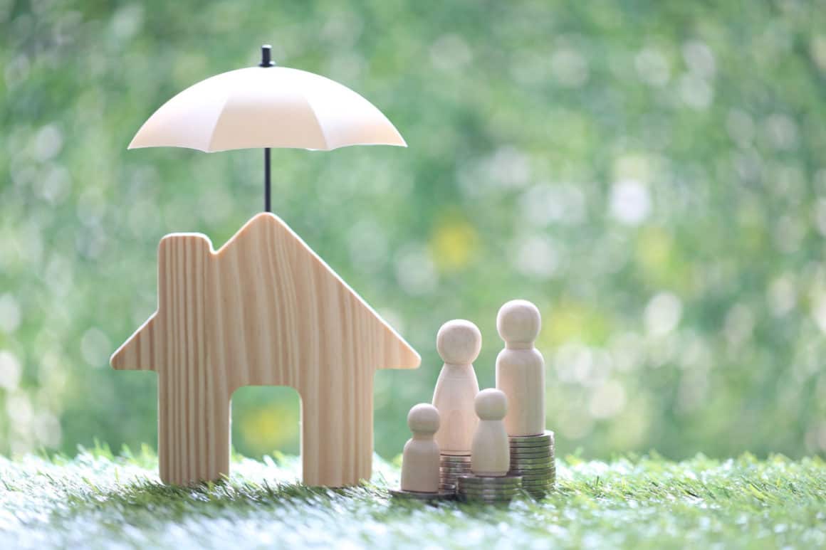 Découpe de maison en bois avec un parapluie au dessus et des membres de la famille à côté, connotant la protection de l'immobilier.